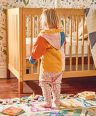 modern toddler hoodie on toddler girl in bedroom with floral wallpaper and light wooden crib