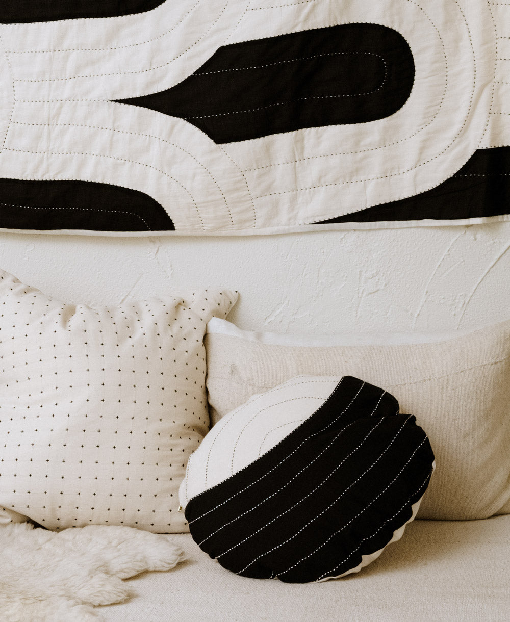 circle pillow in black and white lunar design on all white modern sofa with black and white tapestry in background