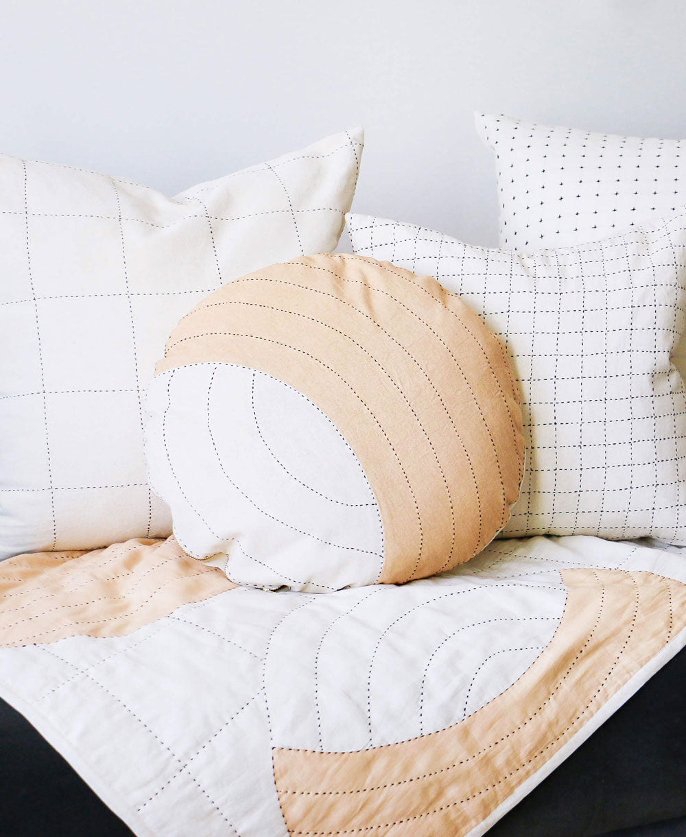 Quilted beige and white pillow on a bed with a neutral background