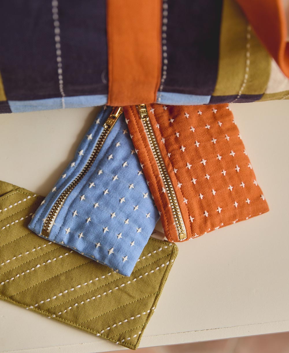 Three fabric pouches with zippers in blue, orange, and green on a neutral background