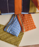 three coin purses in orange, blue and green with white hand-embroidered cross-stitching
