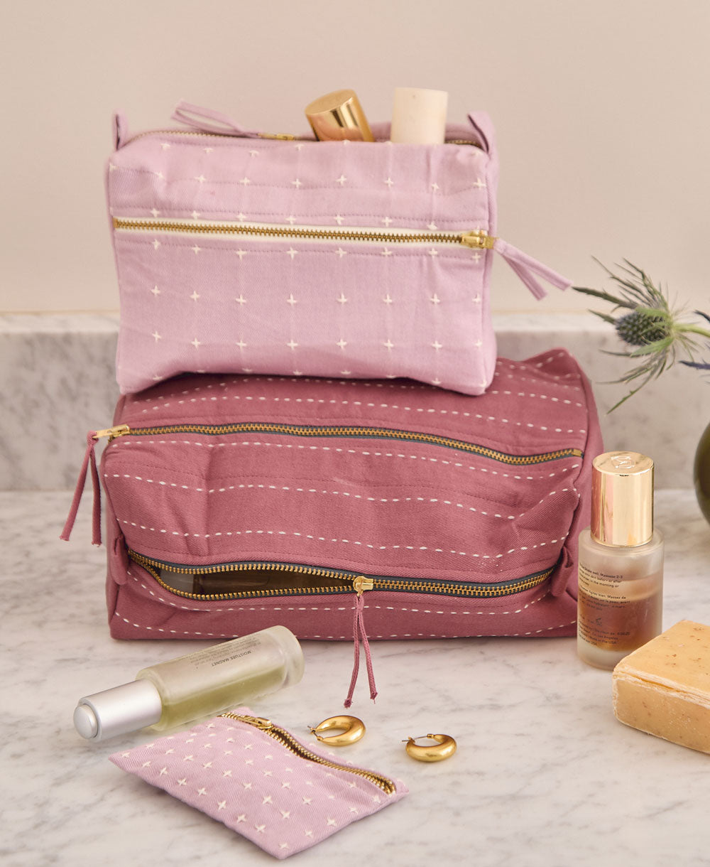 cross-stitch coin purse in lilac sitting on countertop with plum and lilac toiletry bags