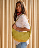 Woman holding a green crescent bag against a beige curtain background