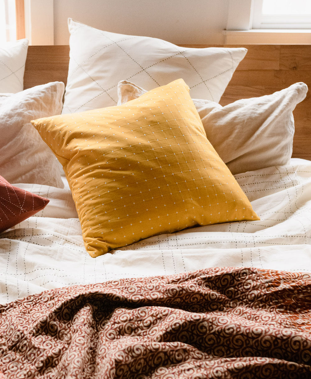 mustard yellow throw pillow on grid bedding with cozy burnt orange kantha quilt on top