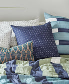 navy blue throw pillow with white cross-stitching on bed with striped sage and navy blanket