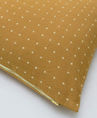 Mustard yellow pillow with white cross pattern on a light gray background