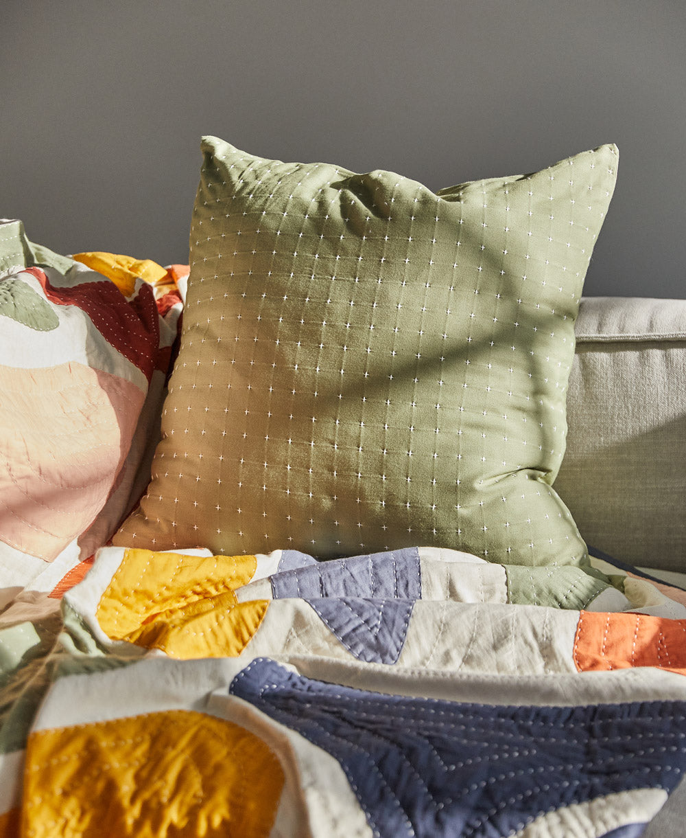 sage green throw pillow on grey sofa with coordinating abstract quilted throw blanket in bold colorful shapes