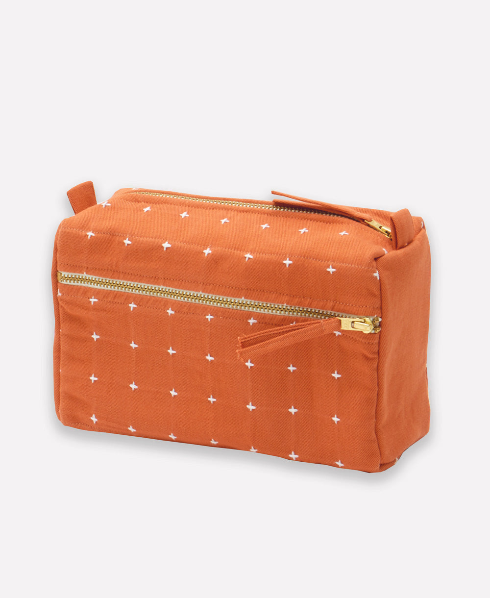 Orange toiletry bag with white cross-stitch patterns on a light gray background