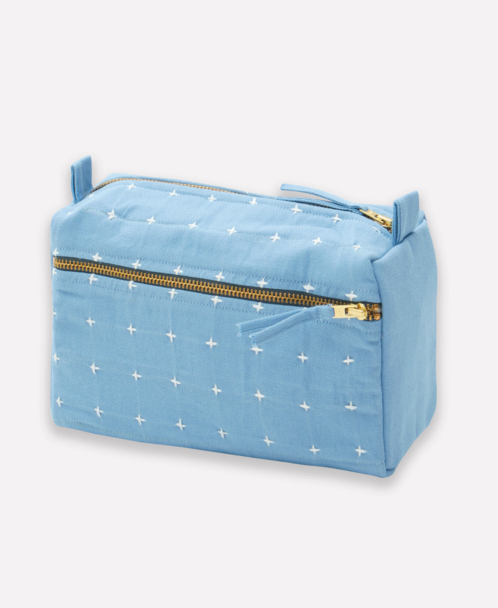 sky blue toiletry bag with whote cross-stitch pattern and gold zipper closure