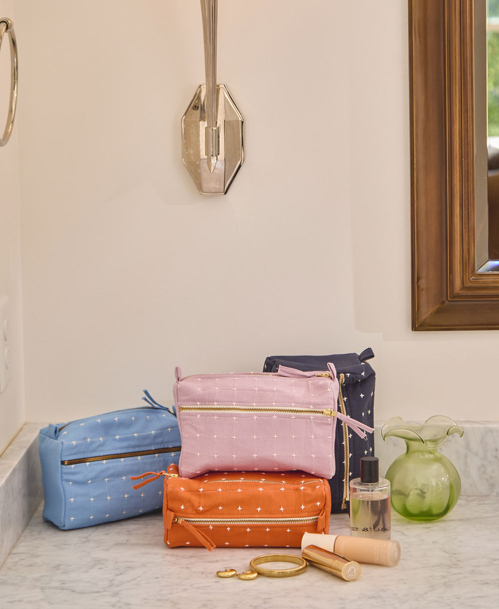 pile of colorful toiletry bags with white cross-stitch design sitting on a gray counter in a bathroom