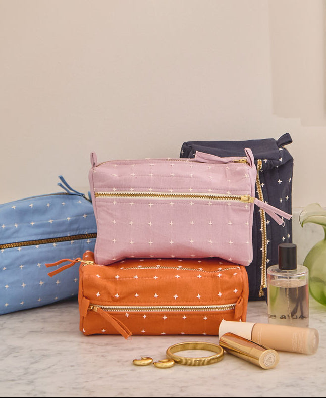 pile of colorful toiletry bags with white cross-stitch design sitting on a gray counter in a bathroom