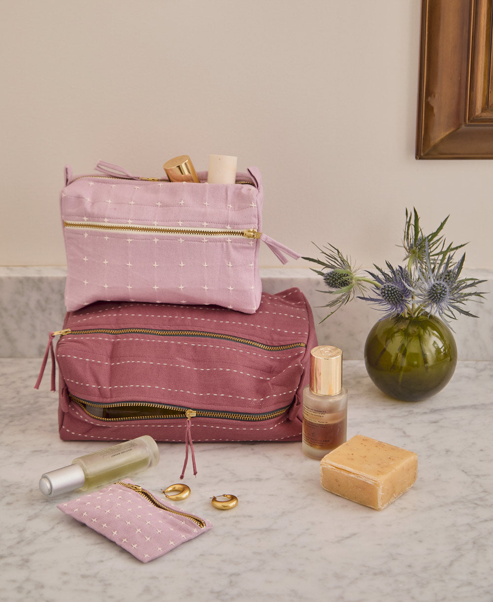 purple and lilac toiletry bags stacked on top of one another on gray countertop in bathroom