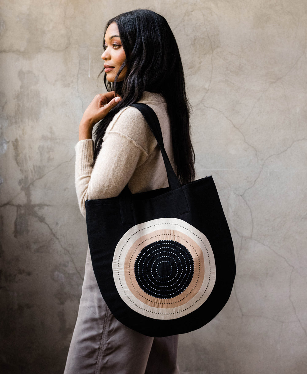 woman carrying curved canvas tote with a modern circular design in black 