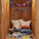 Colorful knitted bunting hanging above a wooden bench with cushions and fabric.