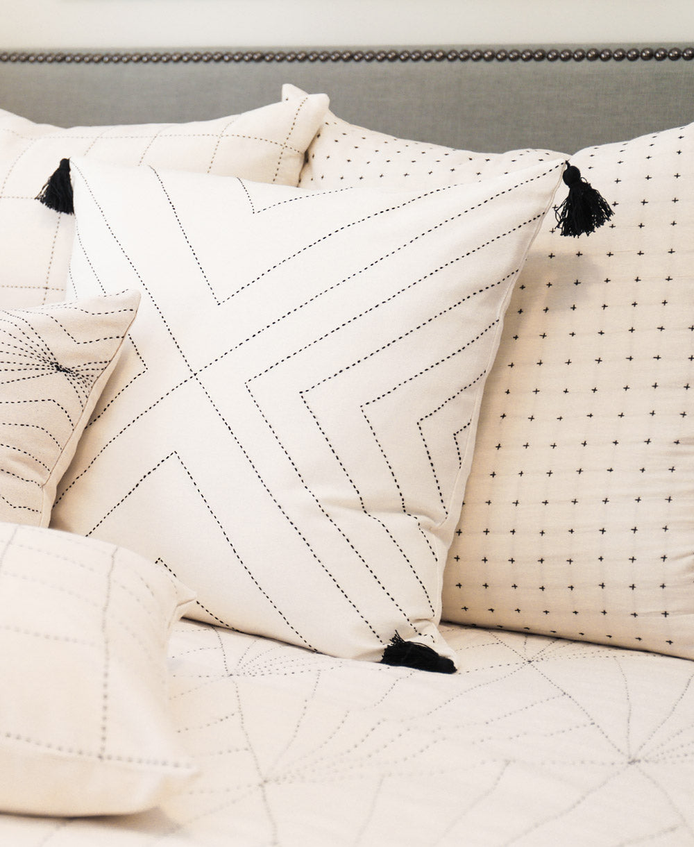 geometric stitch throw pillow on all white bed with other white pillows