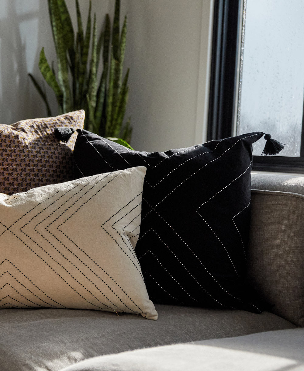 black tassel throw pillow paired with matching white geometric lumbar pillow on grey sofa with snake plant in background