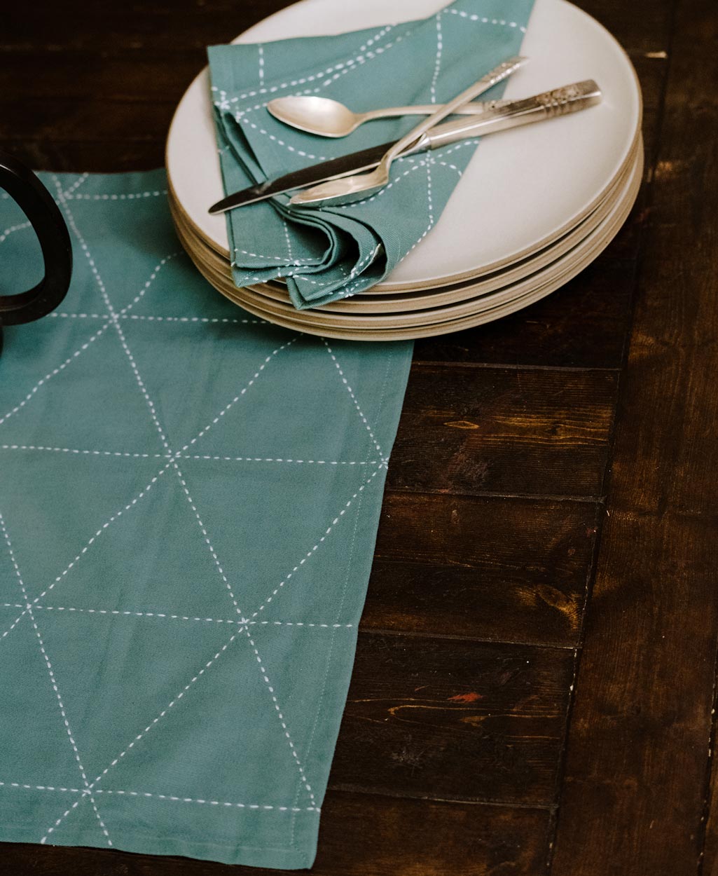 spruce green fabric napkin set on stack of white modern dinner plates atop wooden dining table by Anchal