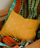 small throw pillow in mustard yellow with white stitching in chair with mismatched vintage kantha quilt