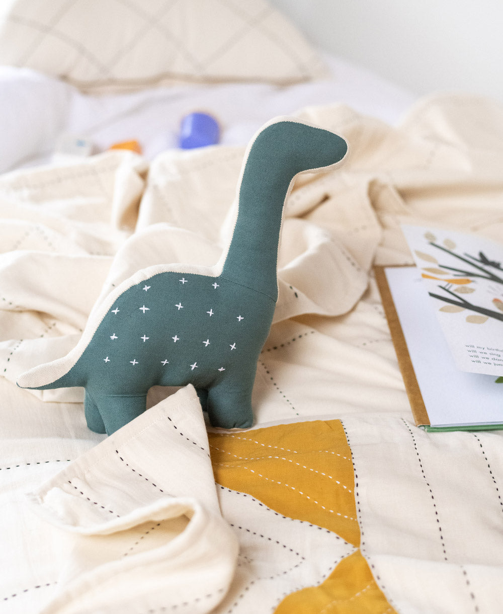 spruce green dinosaur stuffed animal on all white kids bed