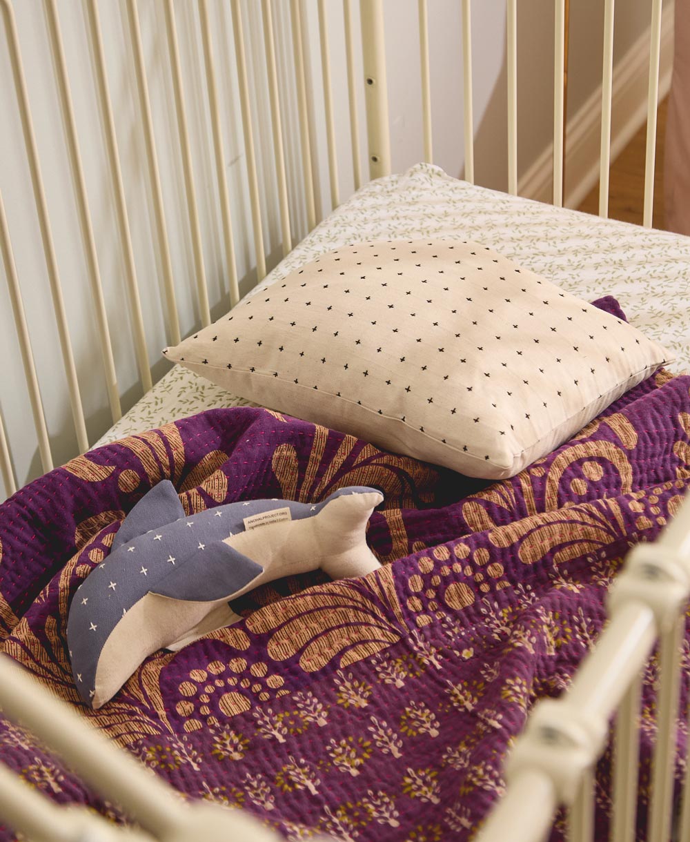 Baby crib with purple and gold blanket, beige pillow, and dolphin stuffed animal