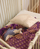 Baby crib with purple and gold blanket, beige pillow, and dolphin stuffed animal