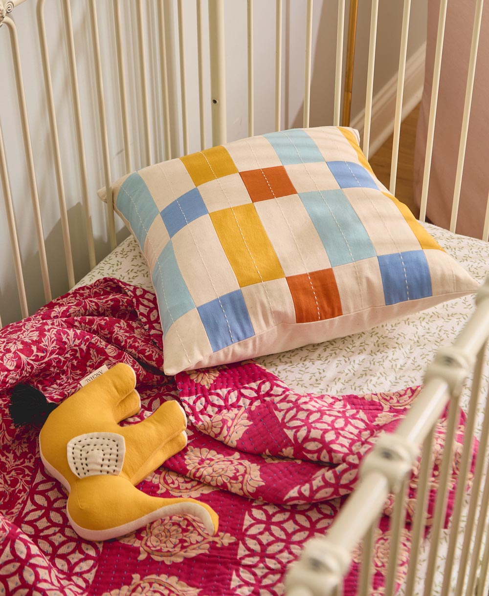 yellow stuffed animal laying on a pink blanket in a white iron crib