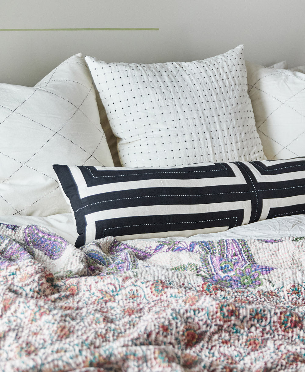 black striped oversized lumbar pillow on bed with white euro shams and modern boho kantha quilt