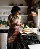 woman in warm white modern kitchen wearing kantha bin apron in red paisley print made in India