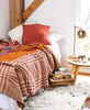 rust and red plaid kantha quilt on all white twin bed with modern table lamp