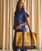woman holding a yellow patterned oversized canvas tote bag in front of ivory curtains