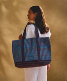 woman carrying a blue patterned tote bag over her shoulder against a beige background