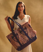 woman holding canvas tote bag in pink paisley against a grey background