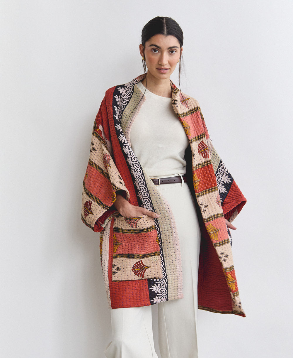 woman wearing unique kantha stitched quilted jacket in shades of red, tan and coral