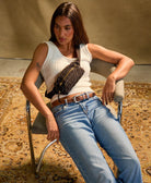 woman sitting in a chair wearing a white top and a black crossbody belt bag