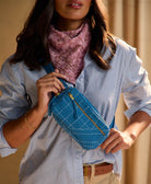woman holding cobalt crossbody belt bag over her shoulder