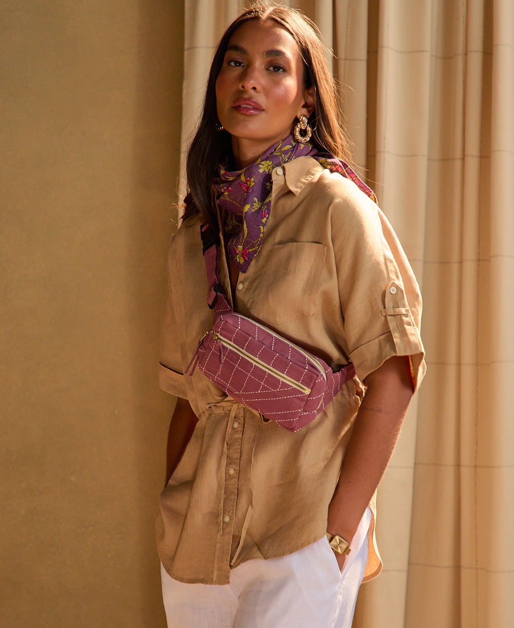 woman wearing berry crossbody belt bag wearing a tan shirt and white pants