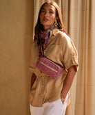 woman wearing berry crossbody belt bag wearing a tan shirt and white pants