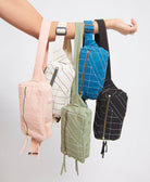Five small belt bags in different colors hanging from a person's arm against a light gray background.