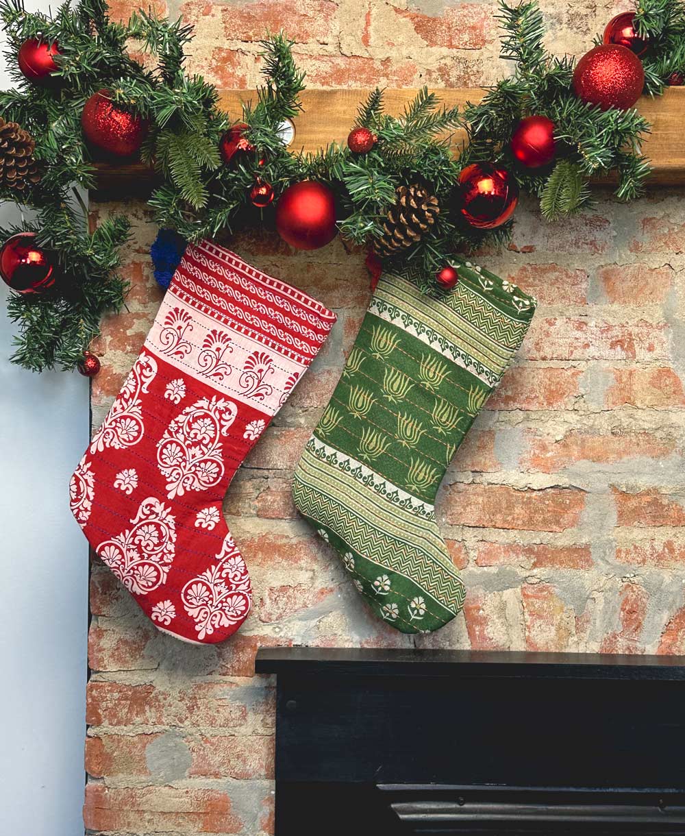 red and green holiday stockings handing from wooden mantel on brick fireplace by Anchal