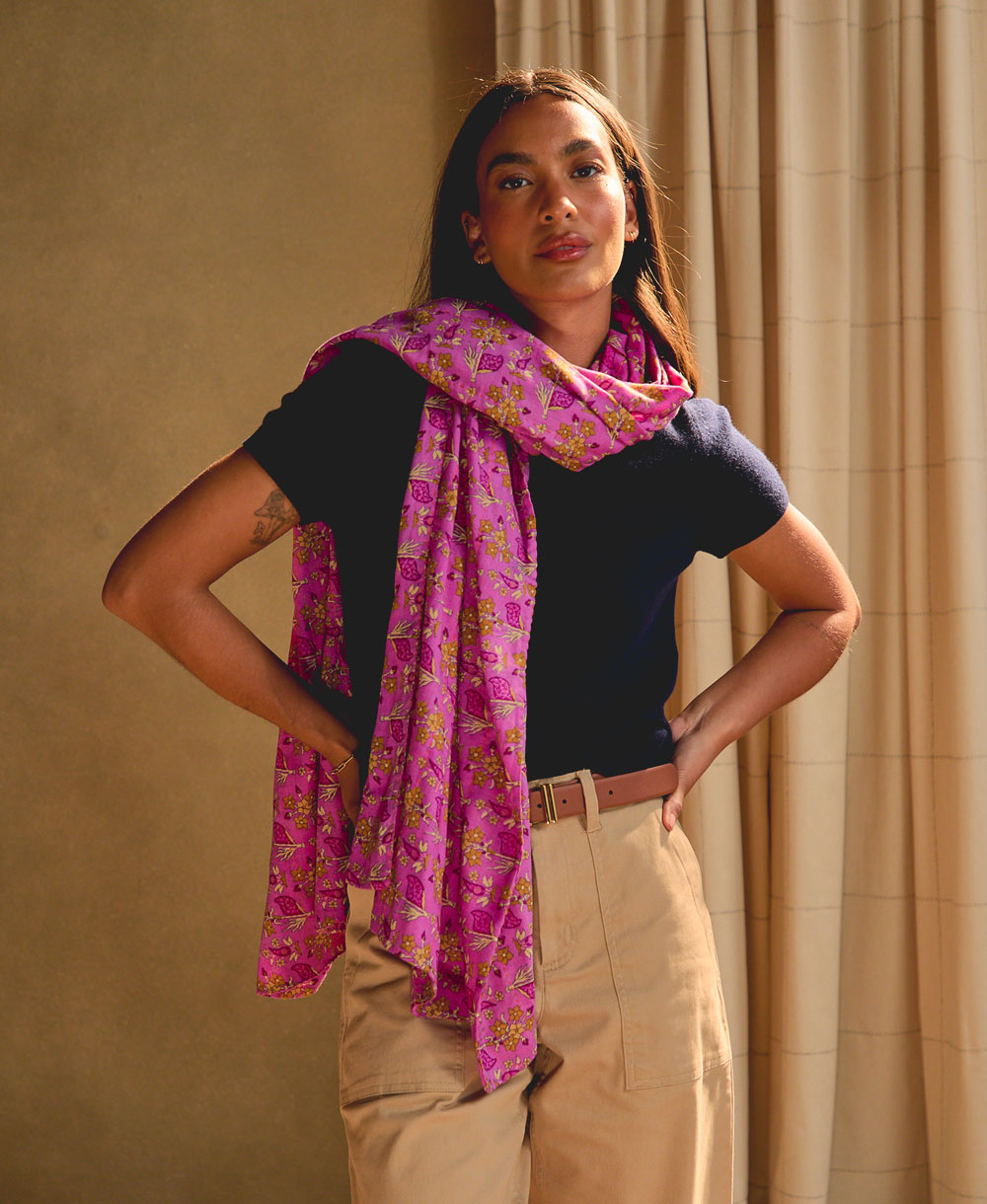 woman wearing a hot pink floral long cotton scarf against a beige background with ivory curtain panels
