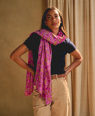 woman wearing a hot pink floral long cotton scarf against a beige background with ivory curtain panels