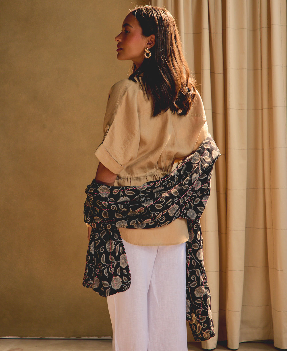 woman wearing a black and grey floral long cotton scarf against a beige background with ivory grid-stitch curtains