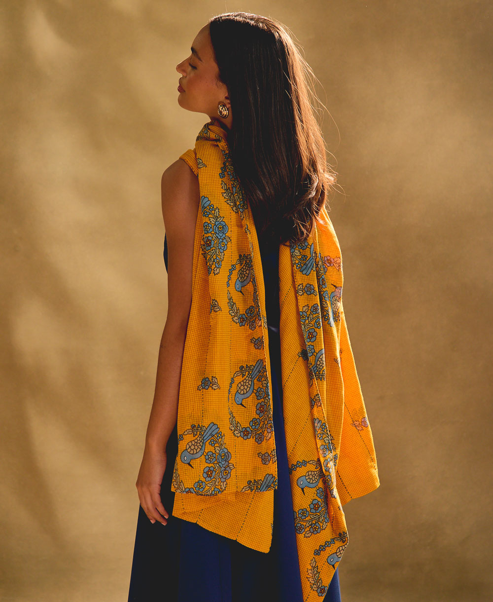 woman wearing long cotton scarf in orange with blue floral print against a beige background