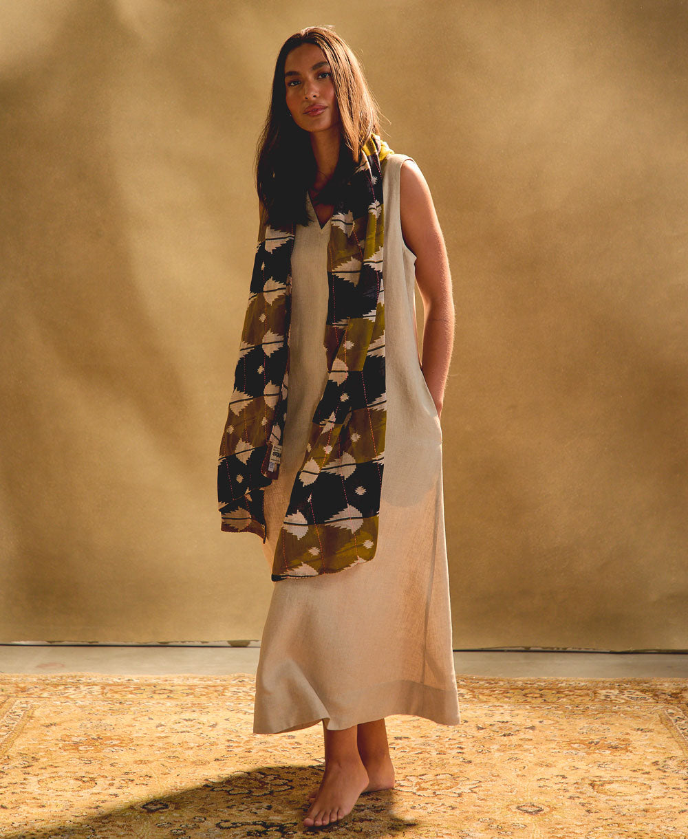 woman wearing an olive green and navy blue long cotton scarf with a light linen dress against a beige background