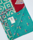 teal kantha quilt throw with a tag featuring the hand-stitched signature of the maker