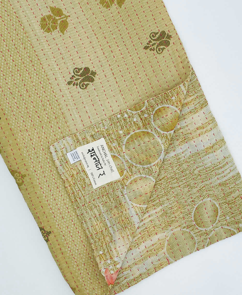 green kantha quilt throw with a tag featuring the hand-stitched signature of the maker