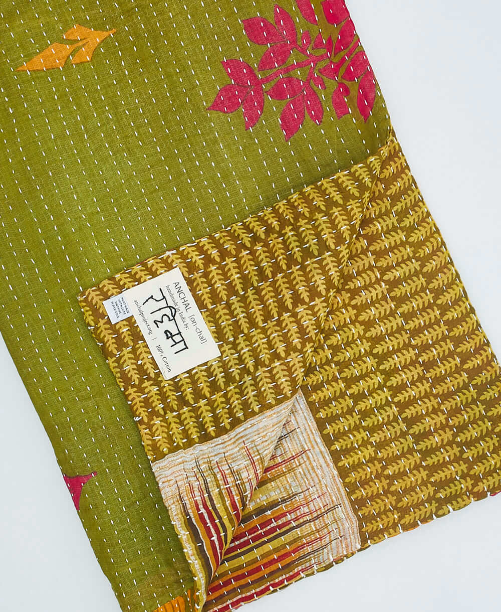 Green kantha quilt throw with a tag featuring the hand-stitched signature of the maker