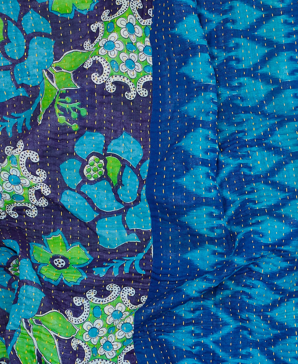 Blue kantha quilt throw with a tag featuring the hand-stitched signature of the maker