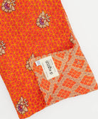 diamond print bright orange kantha quilt throw with a tag featuring the hand-stitched signature of the maker