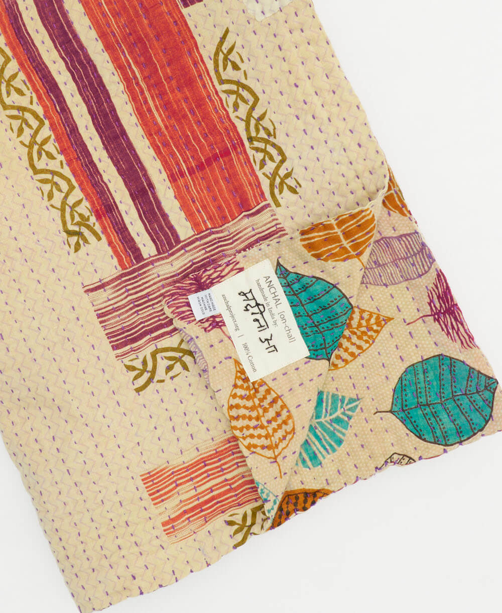 abstract leaf orange & purple kantha quilt throw with a tag featuring the hand-stitched signature of the maker